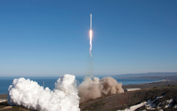 A space rocket launches from a coastal launch pad.